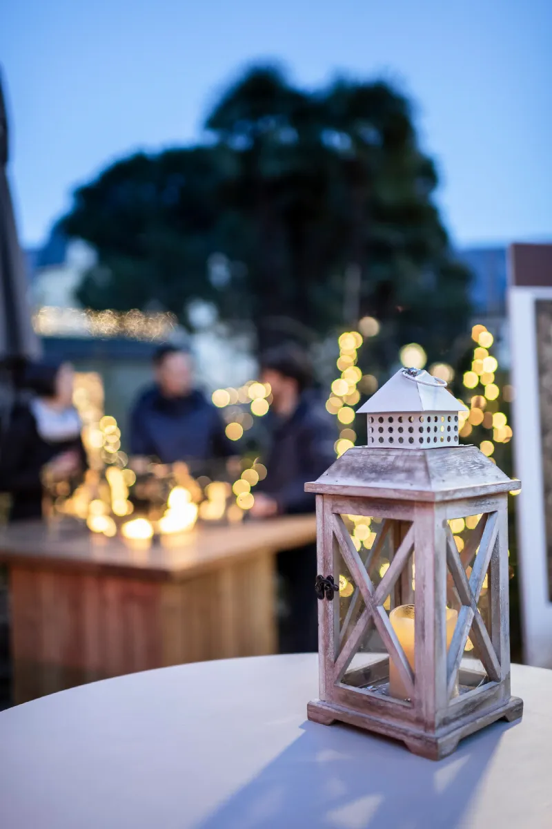 Laterne auf einem Tisch vor einem Weihnachtsmarkt in Bozen mit Menschen und Lichterdekoration im Hintergrund